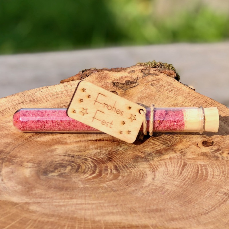Das Bild zeigt ein Reagenzglas mit rotem Blütensalz und Holzanhänger Frohes Fest als Giveaway zu Weihnachten zum kaufen