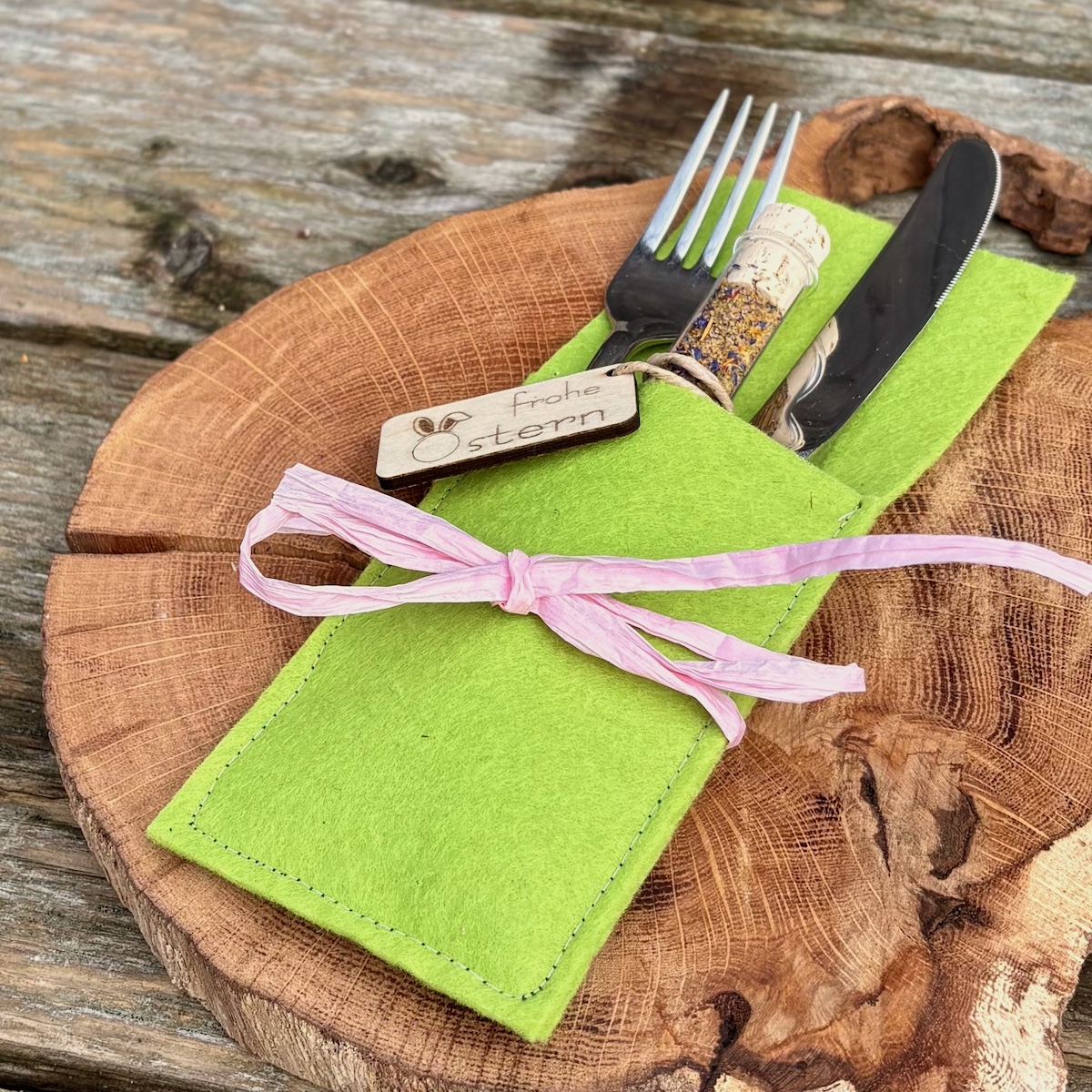 Dekorationsvorschlag Ostersalz im Reagenzglas frohe Ostern in einer Bestecktasche in Frühlingsgrün mit rosa Schleife auf einer Holzscheibe