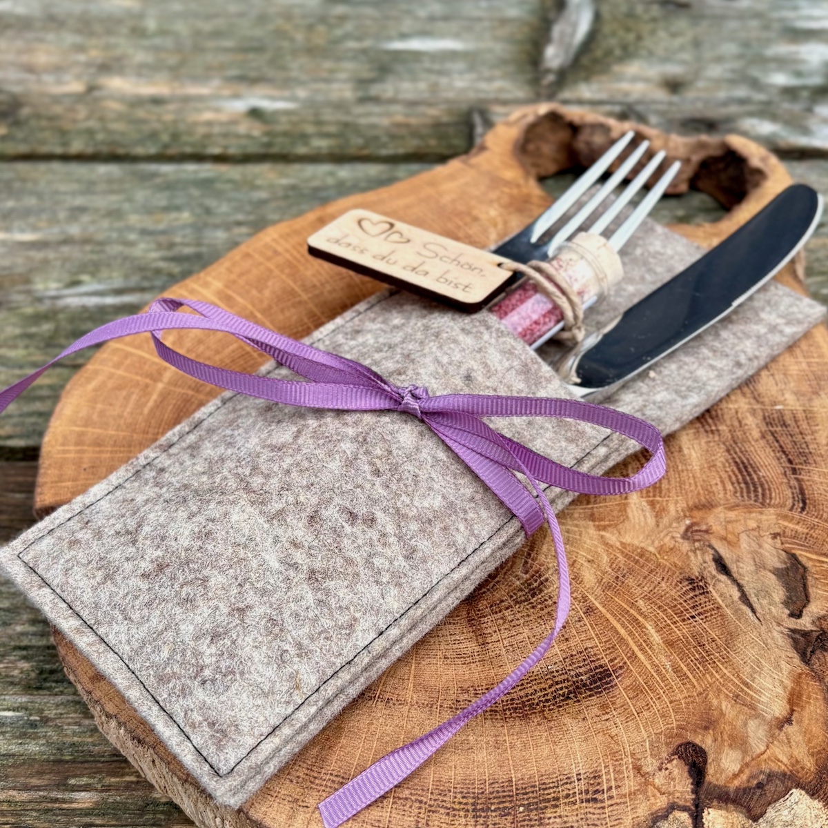 Dekorationsidee Heideblütensalz im Reagenzglas mit Anhänger schön dass du da bist in einer grauen Bestecktasche mit violetter Schleife auf einer Holzscheibe