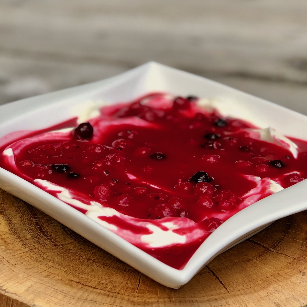 Servierevorschlag Rote Grütze auf Quarkcreme auf weißen Teller auf einem Holzuntergrund