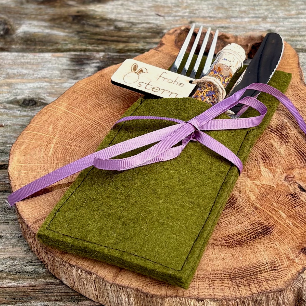 Dekorationsvorschlag Ostersalz im Reagenzglas frohe Ostern in einer Bestecktasche in Dunkelgsgrün mit violetter Schleife auf einer Holzscheibe